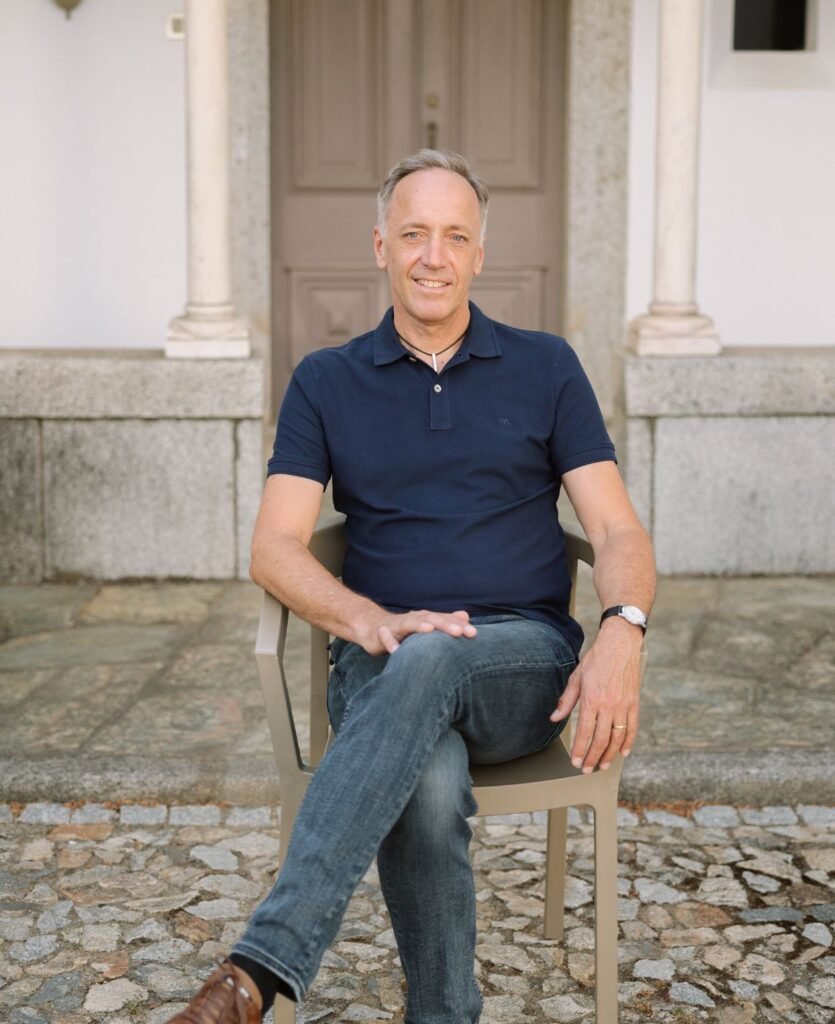 Michael Hertle seated outdoors in front of a stone entrance, presenting a calm and grounded coaching presence.